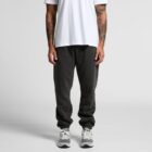Person in white t-shirt, dark joggers, and gray sneakers standing against a plain background.