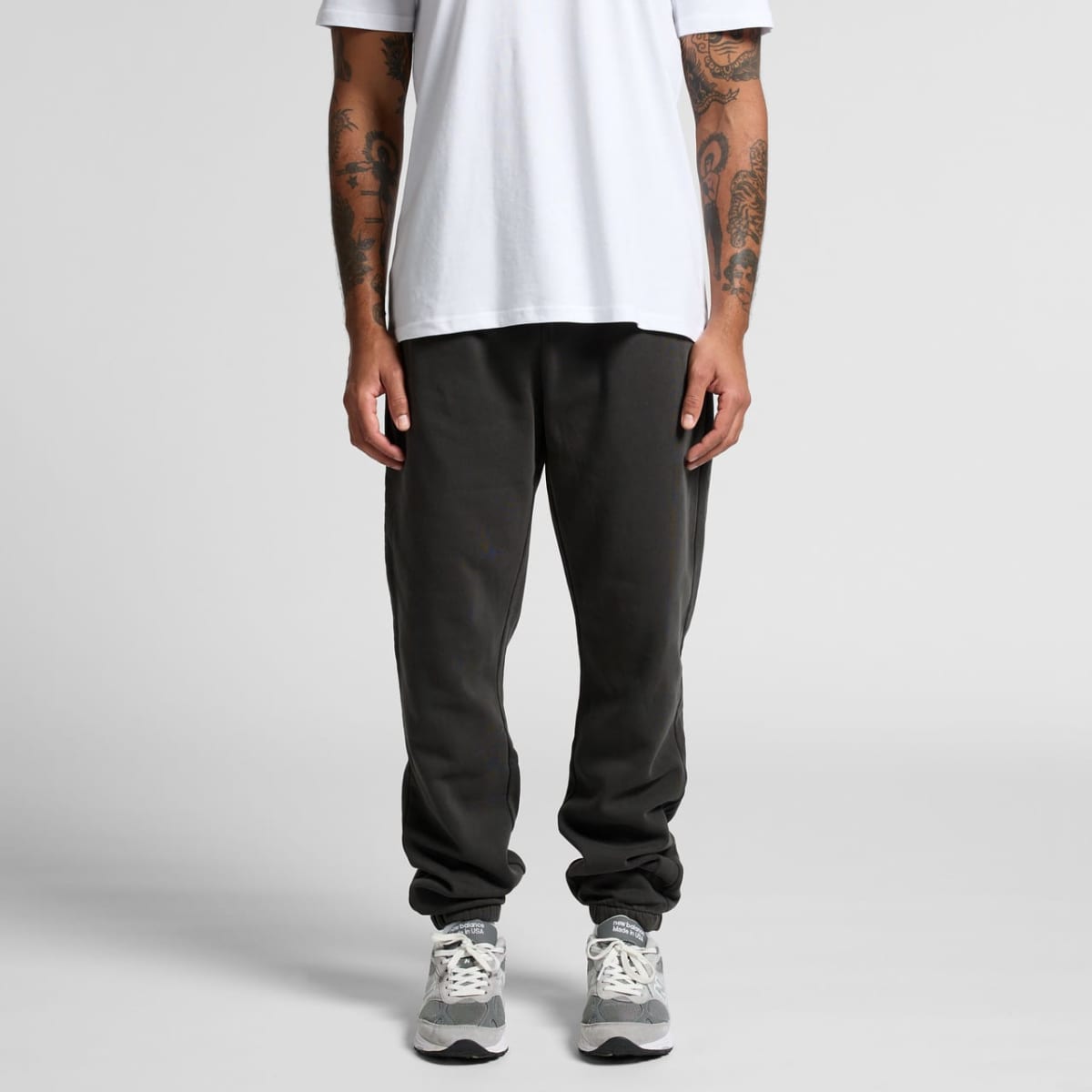 Person in white t-shirt, dark joggers, and gray sneakers standing against a plain background.