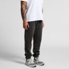 Man in a white t-shirt, black joggers, and gray sneakers standing against a plain background.