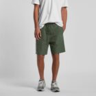 Person wearing a white t-shirt, green shorts, and gray sneakers standing against a plain background.