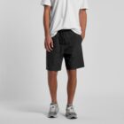 Person wearing a white t-shirt, black shorts, and gray sneakers, standing against a gray background.