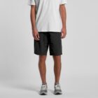 Person wearing a white t-shirt, black shorts, and gray sneakers, standing against a gray background.