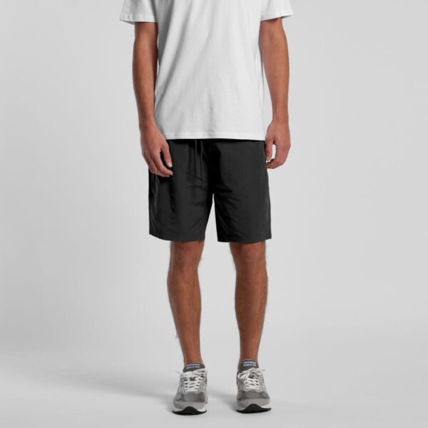Man wearing a white t-shirt, black shorts, and gray sneakers standing against a plain background.