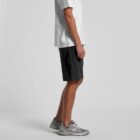 Person in white t-shirt, black shorts, and gray sneakers standing sideways against plain background.