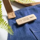 Name tag reading COFFEE CORNER MARIA G. on a denim apron next to green fern leaves.