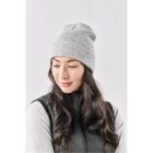 Woman with long hair wearing a gray beanie and jacket, looking down and smiling.