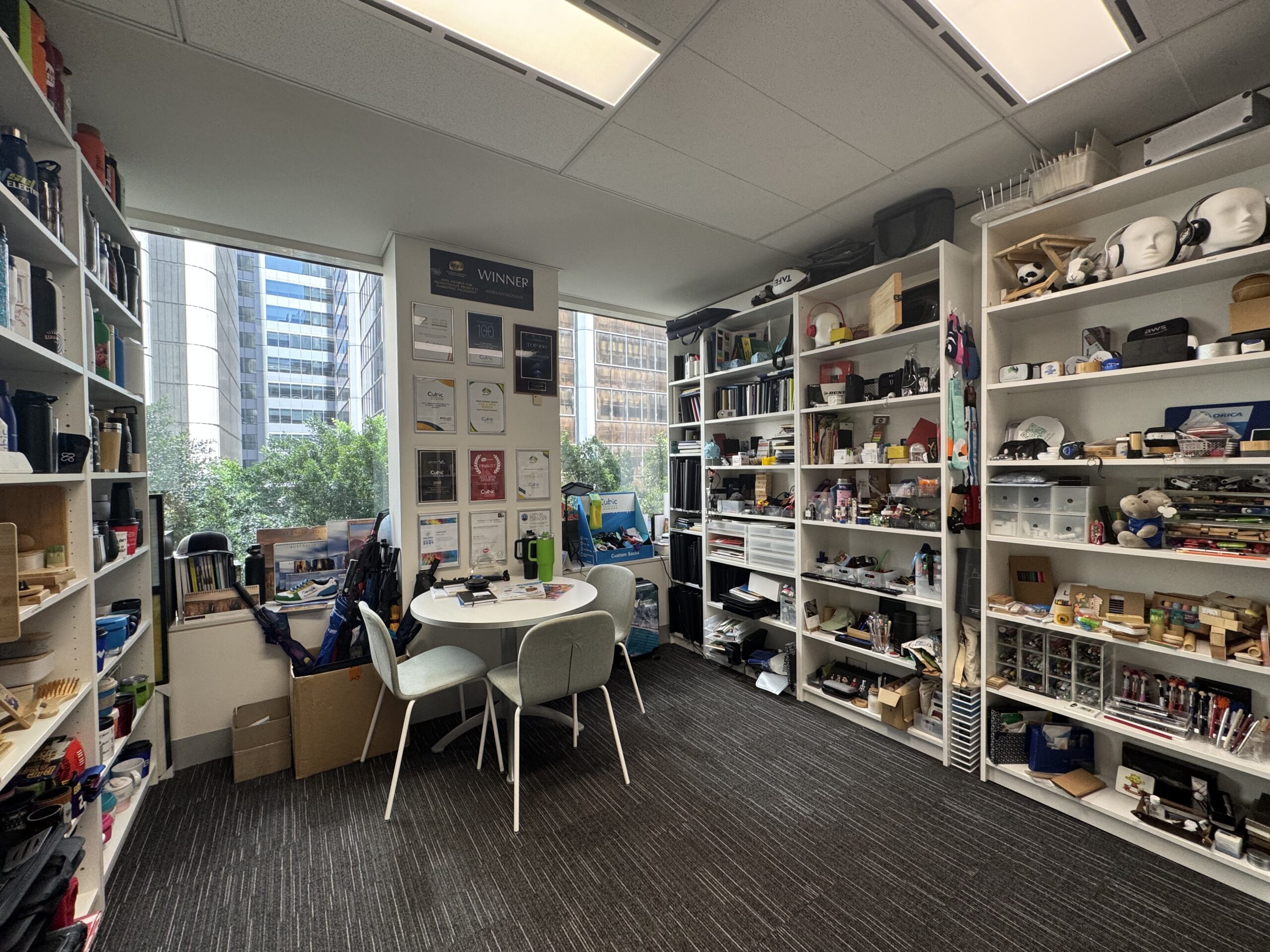 A small office with Cubic Promote shelves, a round table, and large windows facing buildings.