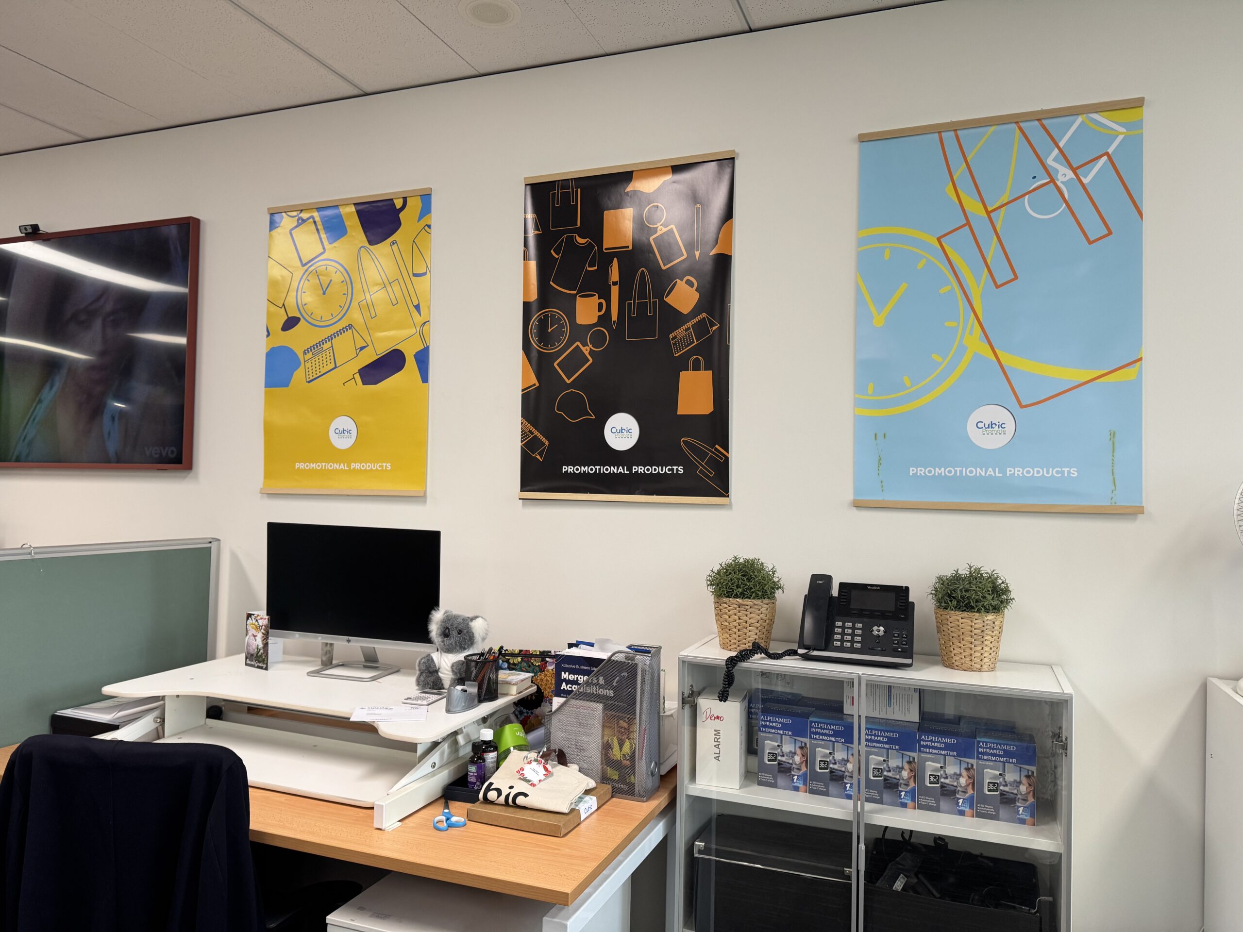 Office workspace with a desk, computer, and three Cubic Promote posters on the wall.