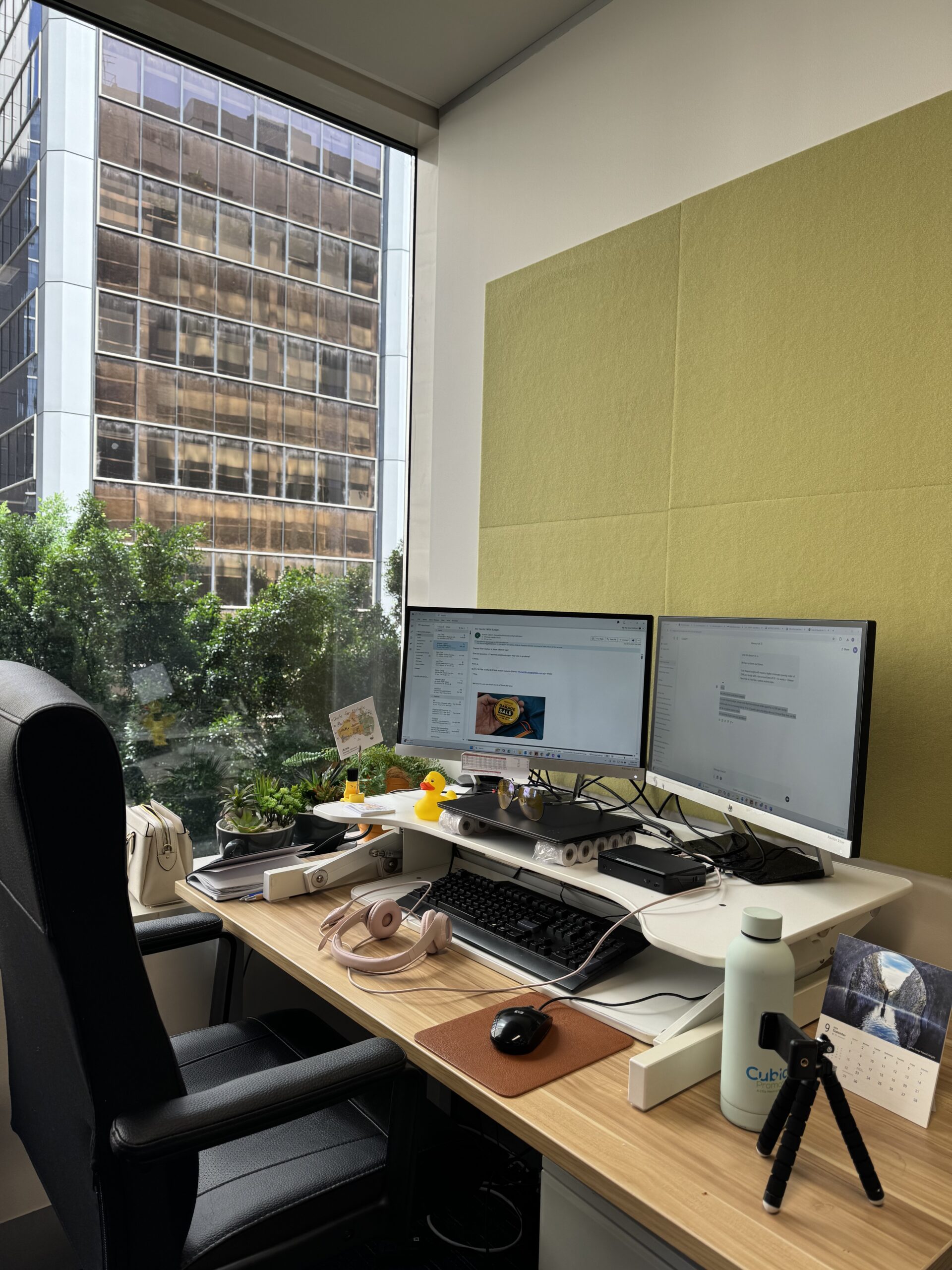 Modern office desk with dual monitors, window view, plants, and Cubic Promote accessories.