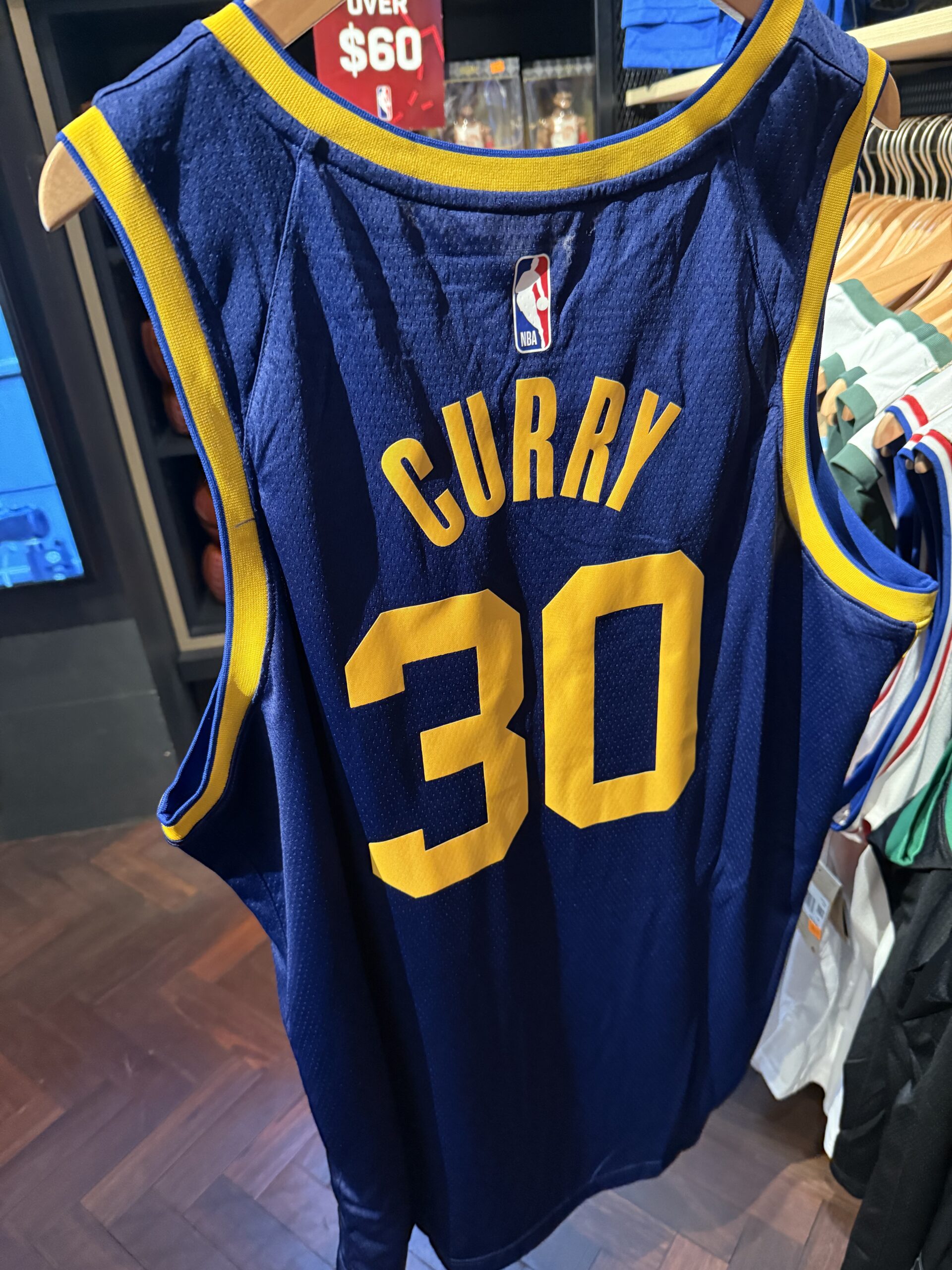Blue and yellow Steph Curry Golden State jersey hanging on a clothing rack in a store.