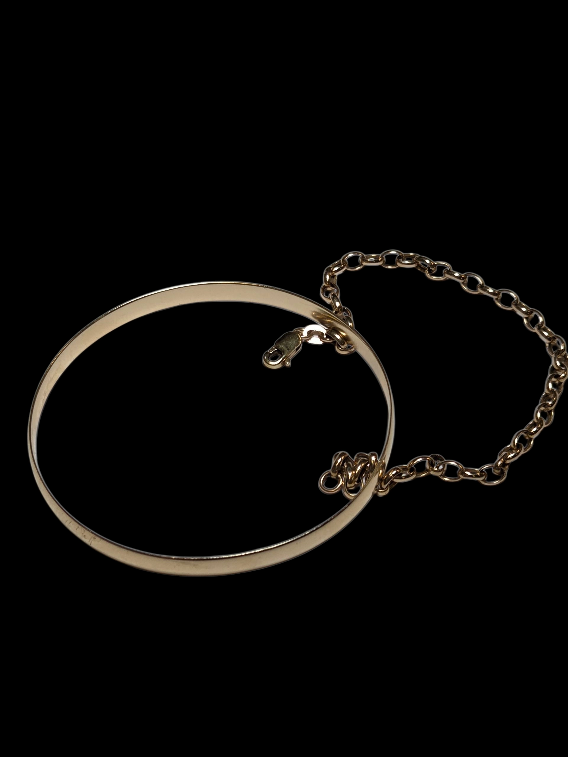 Luxury merchandise: Gold bangle bracelet with a safety chain on a black background.