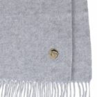 Light gray fringed scarf with a small round metallic emblem on the corner.