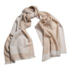 A beige and cream scarf with fringed edges, spread out and loosely knotted.