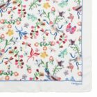 White scarf with colorful floral, butterfly, and bird patterns; blue border; Cacharel logo.
