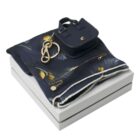 Navy scarf, mini purse, and gold jewelry arranged on a white gift box.