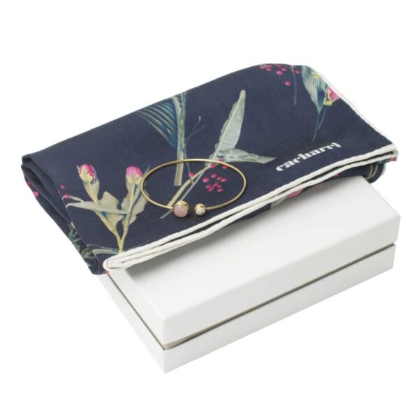 A floral scarf and gold bangle bracelet placed on a white box.