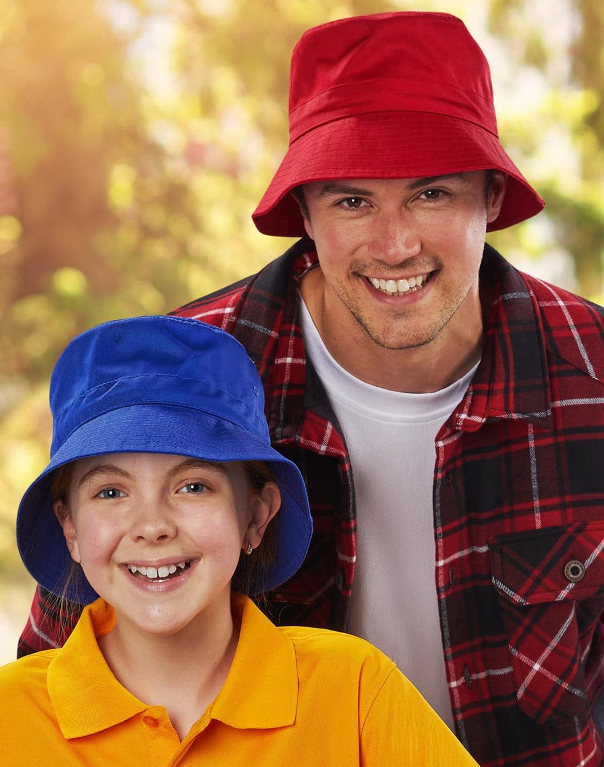 Smiling man in a red bucket hat and girl in a blue bucket hat outdoors.
