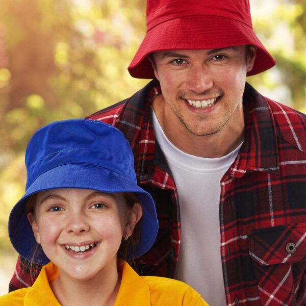 Smiling man in red hat and plaid shirt with girl in blue hat and yellow shirt outdoors.