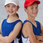 Two kids in blue sports jerseys and hats, smiling with arms crossed, standing back to back.