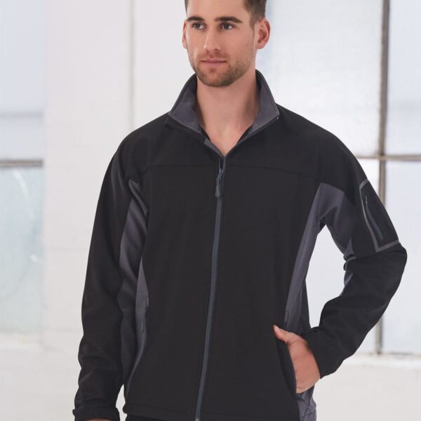 Man in a black and gray zip-up jacket standing indoors with one hand in his pocket.