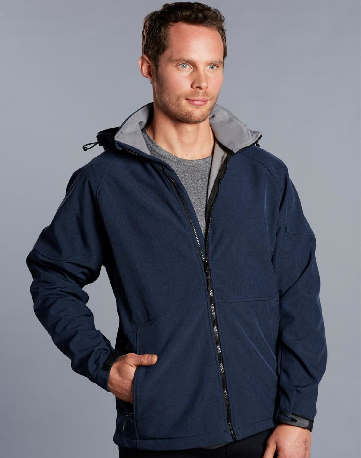 Man wearing a navy blue zip-up jacket with hands in pockets against a plain background.