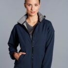 Woman in a navy zip-up jacket with hand in pocket, standing against a gray background.