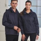 A man and woman wearing navy jackets stand indoors by large windows.