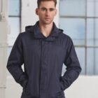 Man in a navy jacket standing indoors with hands in pockets, looking at the camera.