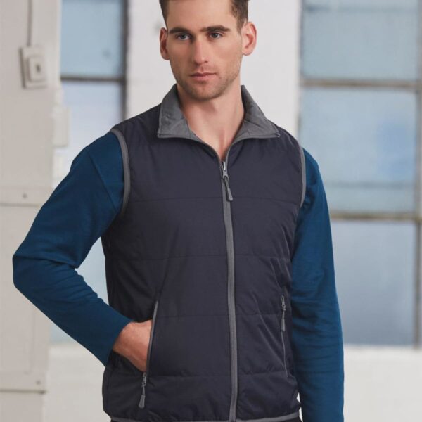 Man wearing a navy blue zip-up vest over a blue long-sleeve shirt, standing indoors.