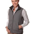 Smiling woman in a gray vest, striped shirt, and tan pants posing with hands in pockets.