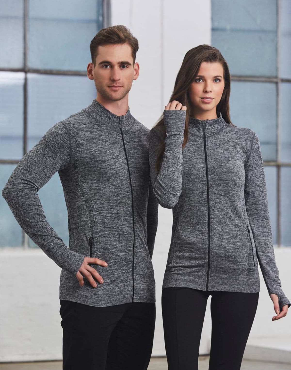 Two people wearing matching gray zip-up jackets and black pants, standing indoors.