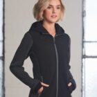 Woman with short blonde hair wears a black zip-up hoodie, standing indoors by windows.