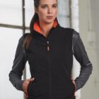 Woman in a black zip-up jacket with gray sleeves, standing indoors by a window.