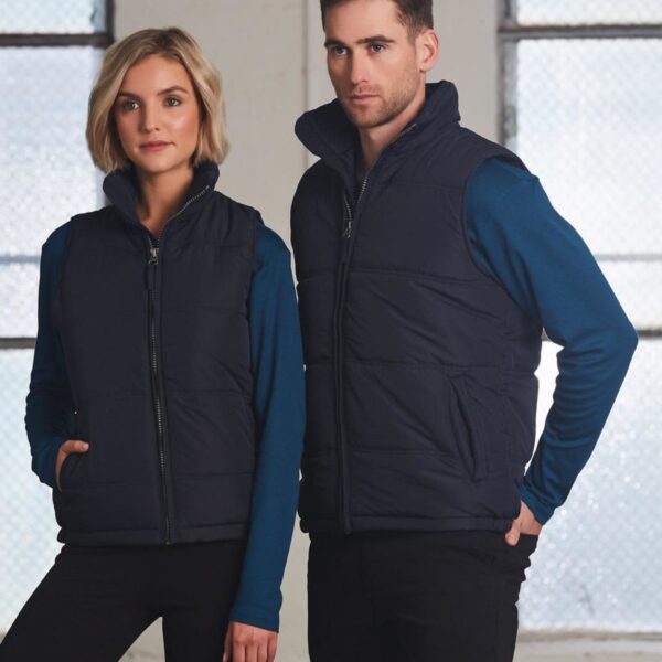 Two people wearing navy vests and blue long-sleeve tops standing indoors.