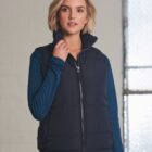 Woman in a navy puffer vest and blue long-sleeve shirt standing indoors.