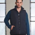 Man wearing a navy puffer vest over a blue long-sleeve shirt, standing indoors.