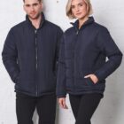 Man and woman in navy puffer jackets stand against a white wall, posing together.