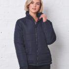 Woman wearing a dark puffer jacket standing against a white brick wall.