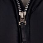 Close-up of a metal zipper on a black fabric garment, partially unzipped.