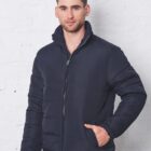 Man in a navy blue puffer jacket standing against a white textured wall.
