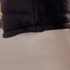 Close-up of the hem of a black puffer jacket against a light background.