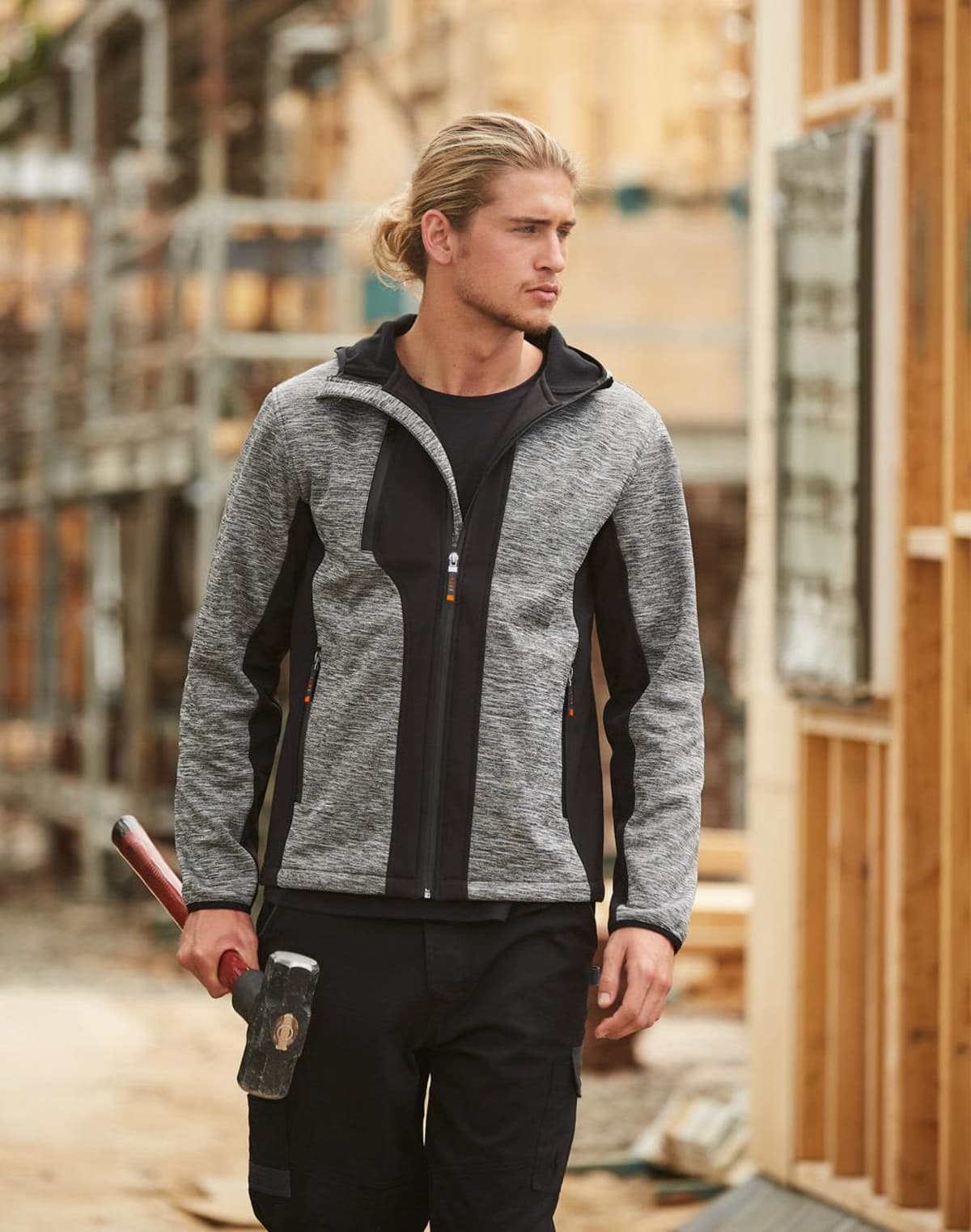 Man in a gray jacket holding a sledgehammer at a construction site.