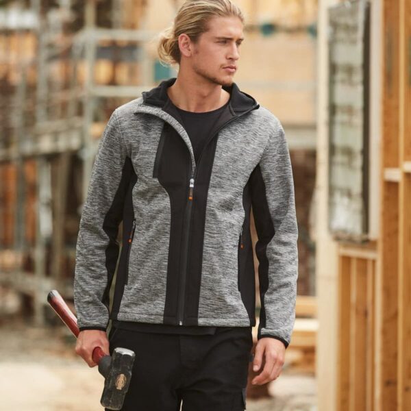 Man in a gray jacket holding a hammer at a construction site.