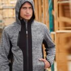 Man in a gray hooded jacket standing at a construction site with wooden frames in the background.
