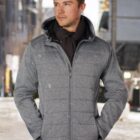 Man in gray jacket and scarf standing outside on a snowy city street.