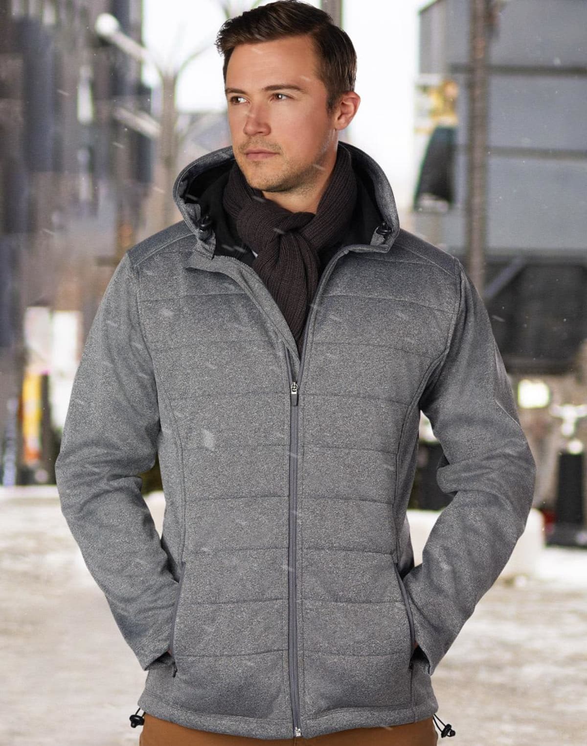 Man in gray jacket and scarf standing outside on a snowy city street.