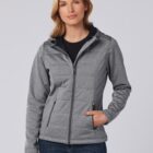 Woman wearing a gray zip-up jacket with a hood and blue jeans, standing against a plain background.