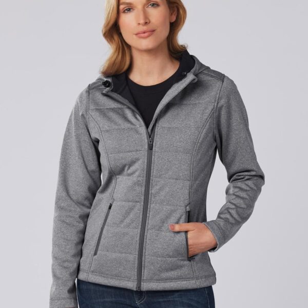 Woman in a gray zip-up jacket with hood, posing with hand in pocket against gray background.