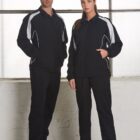 Two people wearing matching black and white tracksuits standing indoors by a window.