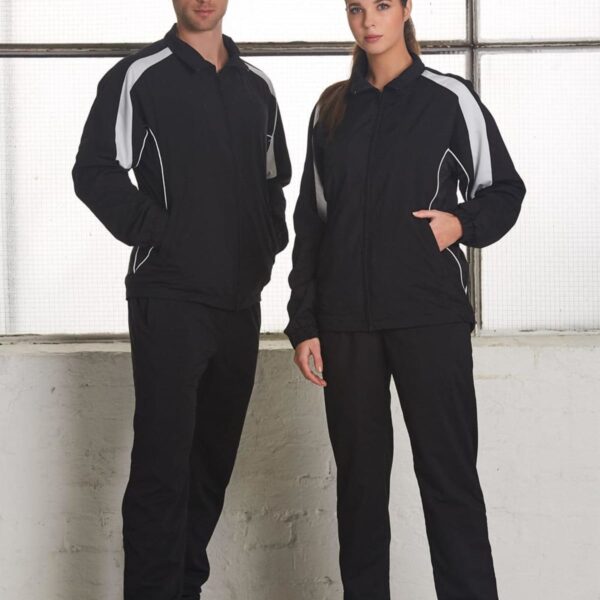 Two people in black and white tracksuits stand indoors near a large window.